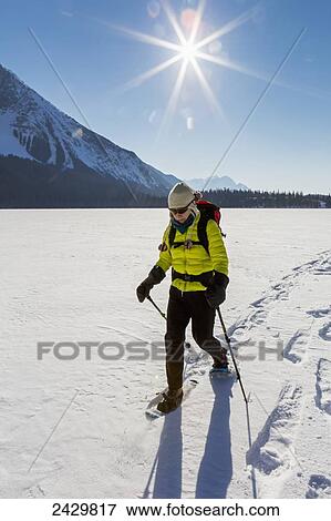 Female snowshoeing on snow covered mountain lake with sunburst and blue sky; Field, British Columbia, Canada View Large Photo Image Stock Photo - Female snowshoeing on snow covered mountain lake with sunburst and blue sky; Field, British Columbia, Canada. Fotosearch