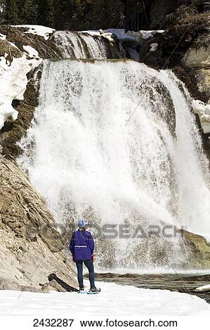 Female snowshoer on snow covered river bank looking at waterfalls flowing over rocks; Field, British Columbia, Canada View Large Photo Image Stock Photo - Female snowshoer on snow covered river bank looking at waterfalls flowing over rocks; Field, British Columbia, Canada. Fotosearch