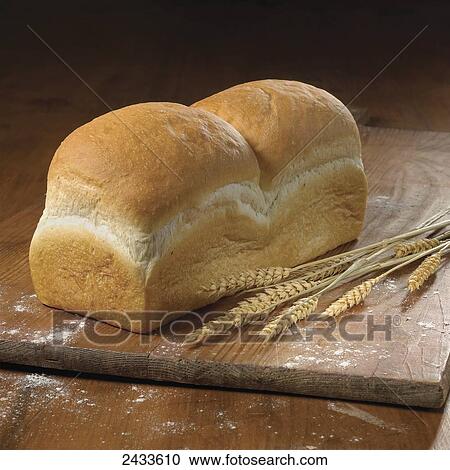 Stock Image - Fresh bread on a wooden cutting board with wheat. Fotosearch