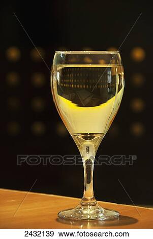 Stock Photo - Glass of white wine on a restaurant wooden table against a black background; Mendoza, Argentina. Fotosearch