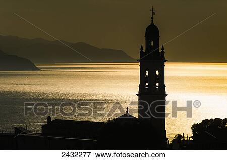 Stock Photo - Golden sunlight reflected on water at dusk with tower of church; San Lorenzo della Costa, Liguria, Italy. Fotosearch