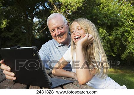 Grandfather and granddaughter looking at a tablet together in a park; St. Albert, Alberta, Canada View Large Photo Image Stock Photo - Grandfather and granddaughter looking at a tablet together in a park; St. Albert, Alberta, Canada. Fotosearch