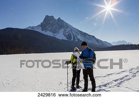 Male and female snowshoeing on snow covered mountain lake looking at map with sunburst and blue sky; Field, British Columbia, Canada View Large Photo Image Stock Photograph - Male and female snowshoeing on snow covered mountain lake looking at map with sunburst and blue sky; Field, British Columbia, Canada. Fotosearch