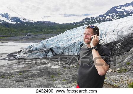 Stock Image - Man talking on a cell phone in front of Shoup glacier, Shoup Bay State Marine Park, Prince William Sound; Valdez, Alaska, United States of America. Fotosearch