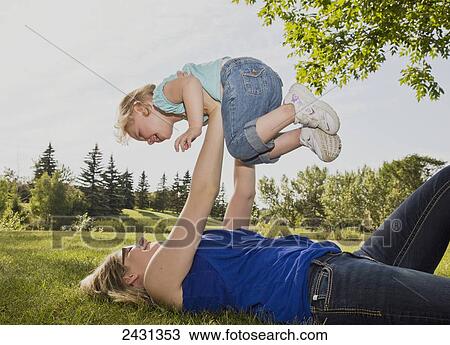 Stock Image - Mother holding her daughter in the air in a park; Edmonton, Alberta, Canada. Fotosearch