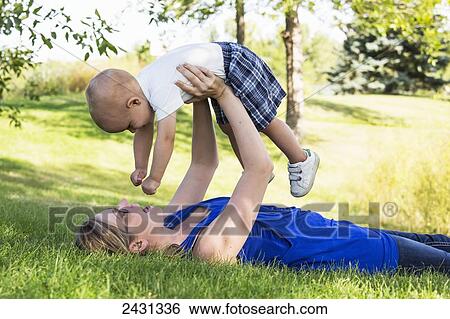 Stock Photograph - Mother holding her young son in the air in a park; Edmonton, Alberta, Canada. Fotosearch
