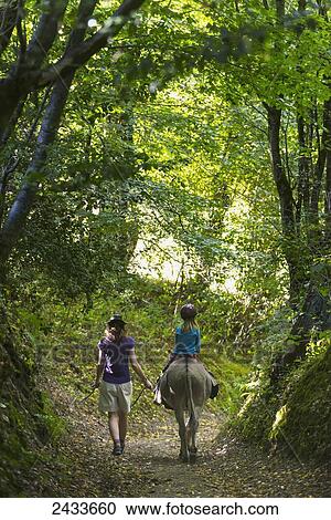 Stock Image - Mother with girl on donkey walking along a trail; Normandy, France. Fotosearch