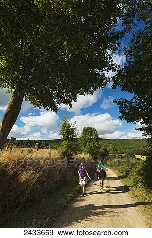 Mother with girl on donkey walking along a dirt road; Normandy, France View Large Photo Image Stock Photo - Mother with girl on donkey walking along a dirt road; Normandy, France. Fotosearch