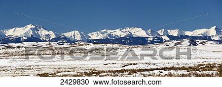 Panarama of snow covered rolling hills with snow covered mountains in the background with blue sky; Longview, Alberta, Canada View Large Photo Image Stock Image - Panarama of snow covered rolling hills with snow covered mountains in the background with blue sky; Longview, Alberta, Canada. Fotosearch