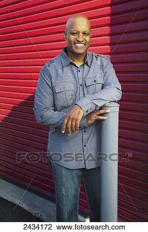 Stock Image - Portrait of a man standing by a red wall; San Francisco, California, United States of America. Fotosearch