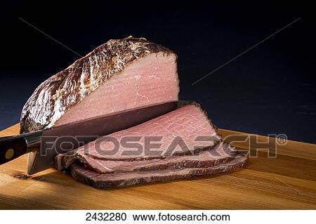 Stock Image - Roast beef being sliced with chef's knife, with slices on top of cutting board; Calgary, Alberta, Canada. Fotosearch