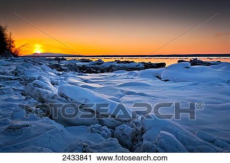 Stock Image - Sunset at Knik Arm in winter, with frozen coast in the foreground; Chugiak, Alaska, United States of America. Fotosearch