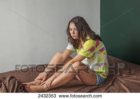 Stock Image - Teenage girl sitting on her bed; Connecticut, United States of America. Fotosearch