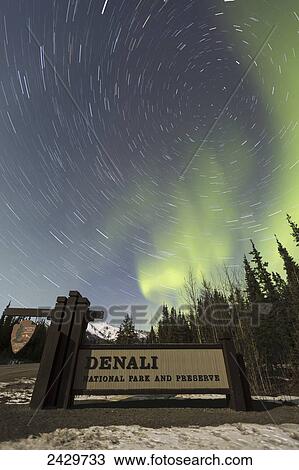 Stock Image - The Aurora Borealis (Northern Lights) and stars circling above the sign marking the entrance to Denali National Park and Preserve; Alaska, United States of America. Fotosearch