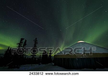Stock Image - The bright neon green aurora illuminates above a yurt in the boreal forest, Chena River State Recreation Area; Fairbanks, Alaska, United States of America. Fotosearch
