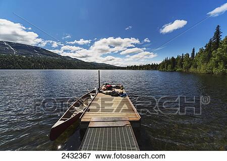 Stock Photo - Three adults and young girl lounging on a boat dock on a lake soaking up the sun, Byers lake campground, Denali State Park; Alaska, United States of America. Fotosearch