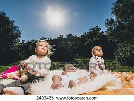 Three young children sit on a blanket at a park looking upwards, with the sunlight shining in the blue sky; Tarifa, Cadiz, Andalusia, Spain View Large Photo Image Stock Photography - Three young children sit on a blanket at a park looking upwards, with the sunlight shining in the blue sky; Tarifa, Cadiz, Andalusia, Spain. Fotosearch