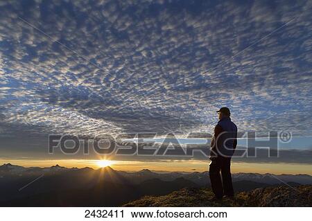 Stock Image - View of Coast Mountains and hiker at sunrise in the alpine on Douglas Island in Alaska's Tongass National Forest, Juneau. Alaska. Fotosearch