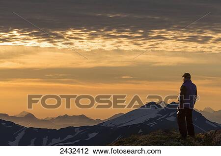 Stock Image - View of Coast Mountains and hiker at sunrise in the alpine on Douglas Island in Alaska's Tongass National Forest, Juneau. Alaska. Fotosearch