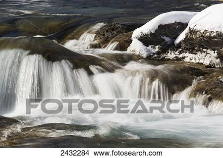 Picture - Water in a river cascading over rocks with snow; Alberta, Canada. Fotosearch