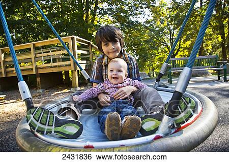 Stock Photograph - Young boy swinging with his baby brother on dish swing at a playground in autumn; Langley, British Columbia, Canada. Fotosearch