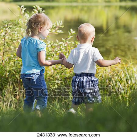 Stock Photo - Young brother and sister walking together on shore; Edmonton, Alberta, Canada. Fotosearch