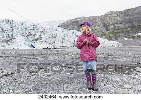 Picture - Young girl dressed in purple standing on morain in front of Shoup glacier, Shoup Bay State Marine Park, Prince William Sound; Valdez, Alaska, United States of America. Fotosearch