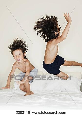 Stock Photo - 5 and 7 year old mixed race boys jumping on a bed; Montreal, Quebec, Canada. Fotosearch