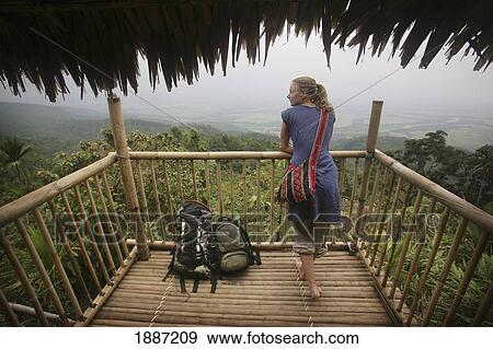 Stock Photo - A Backpacker Woman Standing With Her Rucksack On The Balcony Of A Bamboo Hut Overlooking East Khasi Hills. Fotosearch