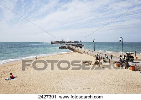 Stock Image - A beach with a long pier out to the water; Cadiz, Andalusia, Spain. Fotosearch