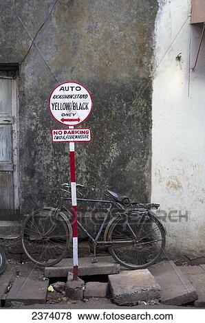 Stock Photo - A bicycle parked outside a building with a rickshaw parking sign; Goa, India. Fotosearch