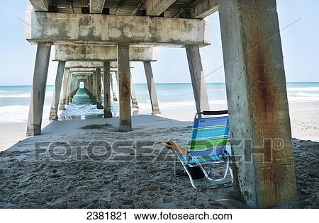 A blue, green, and white striped beach chair sitting empty under a pier on Jupiter Beach; Florida, United States of America View Large Photo Image Stock Image - A blue, green, and white striped beach chair sitting empty under a pier on Jupiter Beach; Florida, United States of America. Fotosearch