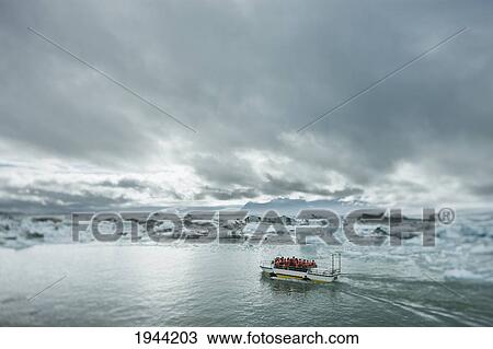 Stock Image - A Boat Full Of People In Orange Life Vests In The Water Traveling Along The Icy Shoreline; Jokulsarlon Iceland. Fotosearch