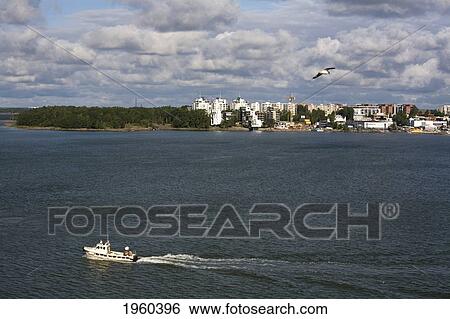 Stock Photograph - A Boat In The Water And Buildings Along The Coastline; Helsinki, Finland. Fotosearch