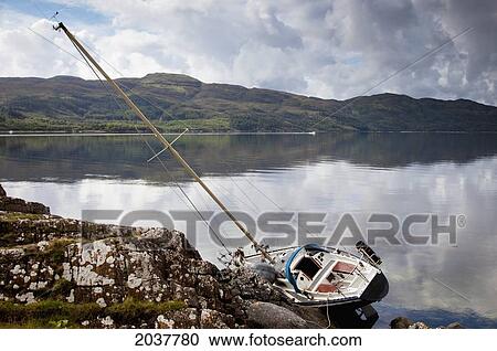 Stock Image - A Boat In The Water Leaning On It's Side Against The Shore; Argyll Scotland. Fotosearch