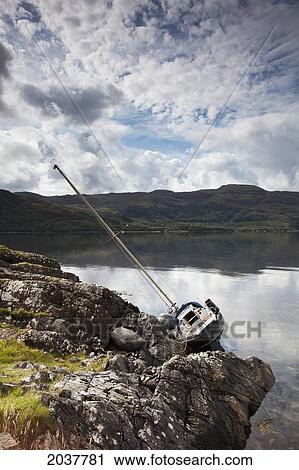 Stock Image - A Boat In The Water Leaning On It's Side Against The Shore; Argyll Scotland. Fotosearch
