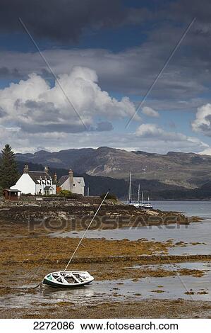 Stock Photograph - A Boat Lays In The Shore At Low Tide With Houses Along The Coastline; Plockton Highlands Scotland. Fotosearch