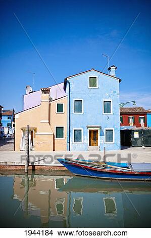 Picture - A Boat Moored Along The Edge Of The Water With Colorful Buildings In The Background; Burano Venezia Italy. Fotosearch