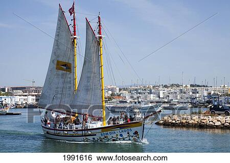 Stock Photograph - A Boat With Large Sails Travels Through The Harbour; Lagos Algarve Portugal. Fotosearch