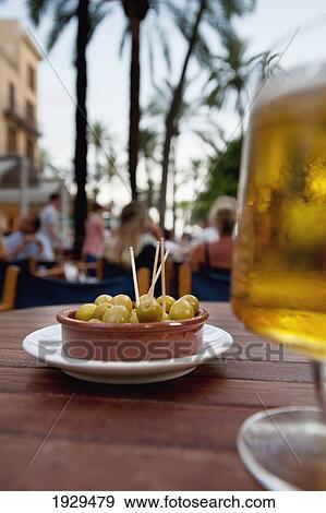 Stock Photo - A bowl of olives and a glass of cold beer on an outdoor patio table; Palma, Majorca, Spain. Fotosearch