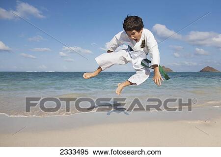 Stock Photography - A boy in a martial arts uniform leaping on a beach; Honolulu, Oahu, Hawaii, United States of America. Fotosearch