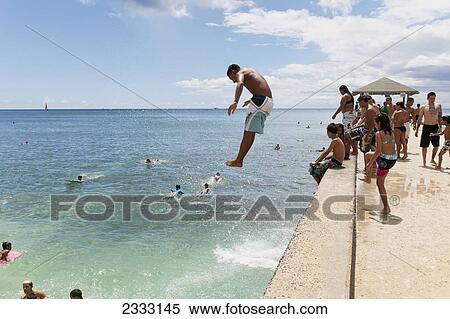 Stock Photography - A boy jumping off the Waikiki Wall; Waikiki, Oahu, Hawaii, United States of America. Fotosearch