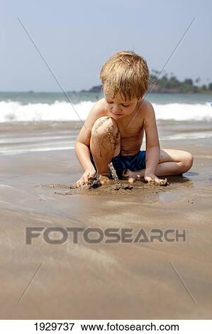Stock Photo - A boy on holiday plays with sand on Patnum beach, Goa, India.. Fotosearch