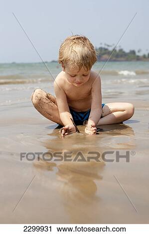 Stock Image - A boy plays with sand on Patnum beach, Goa, India.. Fotosearch