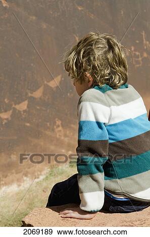 A Boy Sits On The Edge Of A Rock Looking Down Into A Canyon; Arizona United States Of America View Large Photo Image Stock Photo - A Boy Sits On The Edge Of A Rock Looking Down Into A Canyon; Arizona United States Of America. Fotosearch