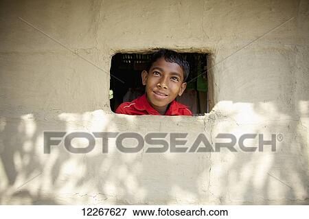 Stock Photo - A boy sticks his head out a small window in a wall; Sunamganj, Bangladesh. Fotosearch