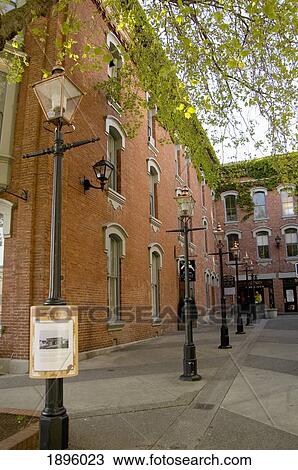 Stock Image - A Brick Building With Windows And Light Posts Along The Sidewalk; Victoria, British Columbia, Canada. Fotosearch