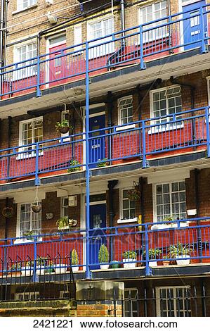 Stock Image - A brick residential building with a blue balcony railings and doors, and a red stripe painted on the lower half of each wall; London, England. Fotosearch