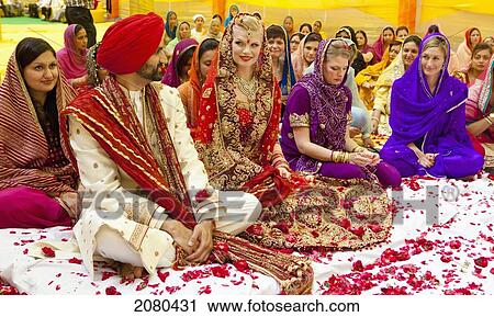 Stock Image - A Bride And Groom Seated In Confetti Amongst Attendants And Guests; Ludhiana, Punjab, India. Fotosearch