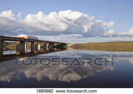 Stock Image - A Bridge Over Red River Floodway With The Clouds Reflected In The River; Winnipeg, Manitoba, Canada. Fotosearch